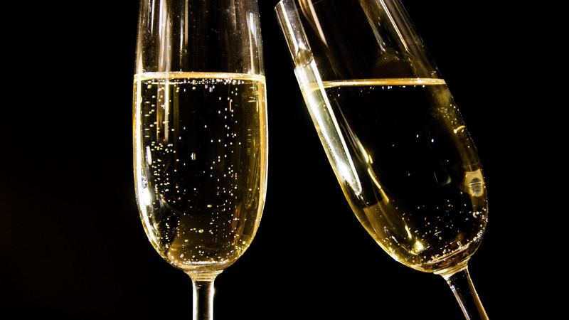 Two flutes of champagne touching against a black background
