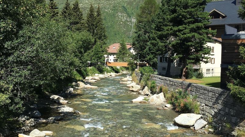 The clear Reuss river running over boulders through Andermatt below green mountains