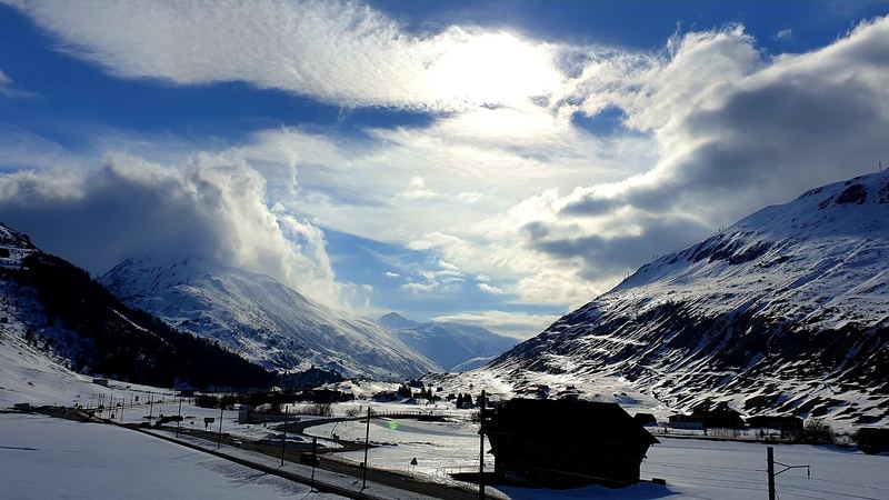 Sun breaking through cloud over the snowy Urseren valley below Andermatt