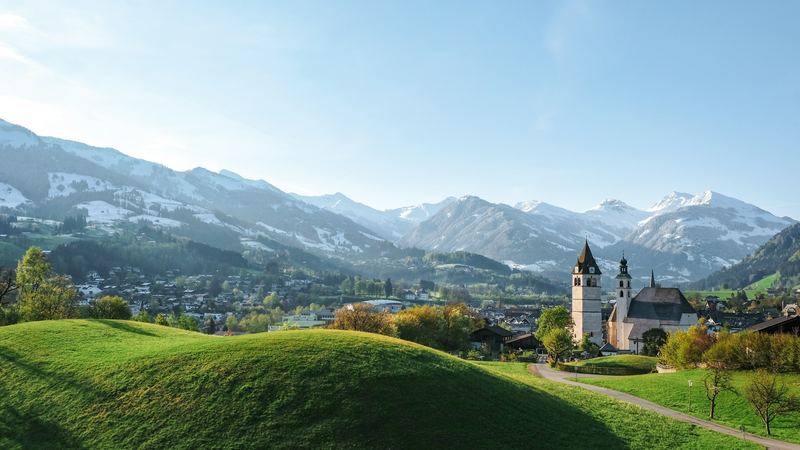 The church of Kitzbühel and green hills below the snow-capped Kitzbühel Alps in spring