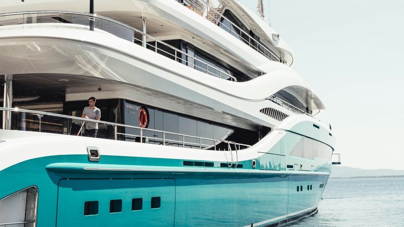The turquoise hull and white decks of a superyacht at anchor