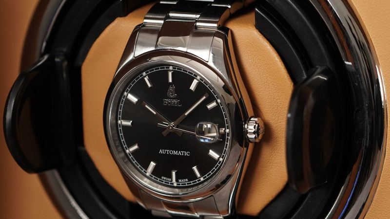 A Swiss automatic watch with a black dial turning in a winder lined in tan leather