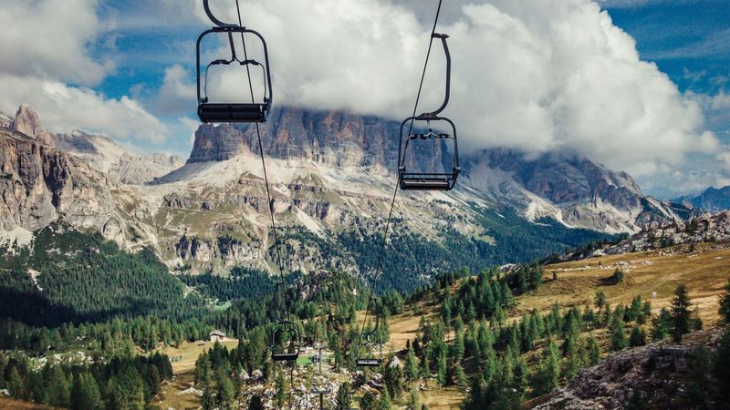 Chairlift seats above larch meadows, the Dolomite walls beyond in the clouds