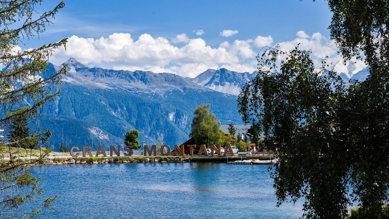 A lake ringed by trees at Crans-Montana, with the mountains of the Valais beyond