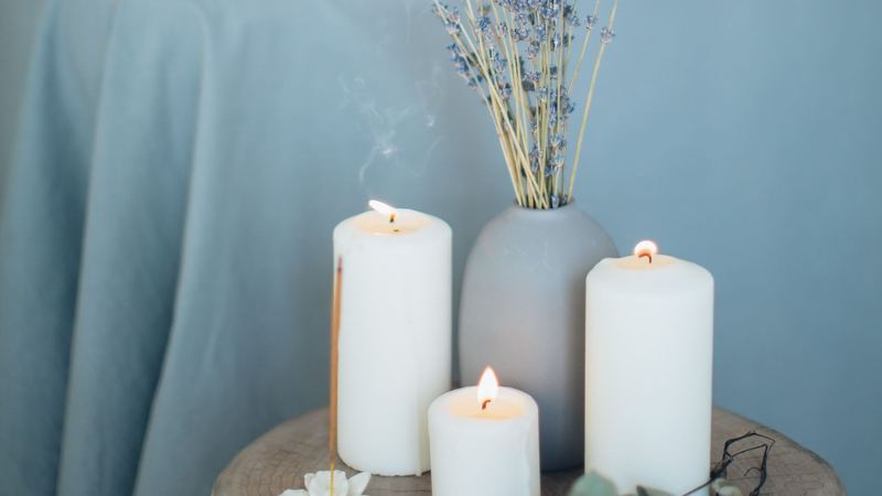Three lit candles, a vase of dried lavender and a stick of incense on a wooden stool in a treatment room