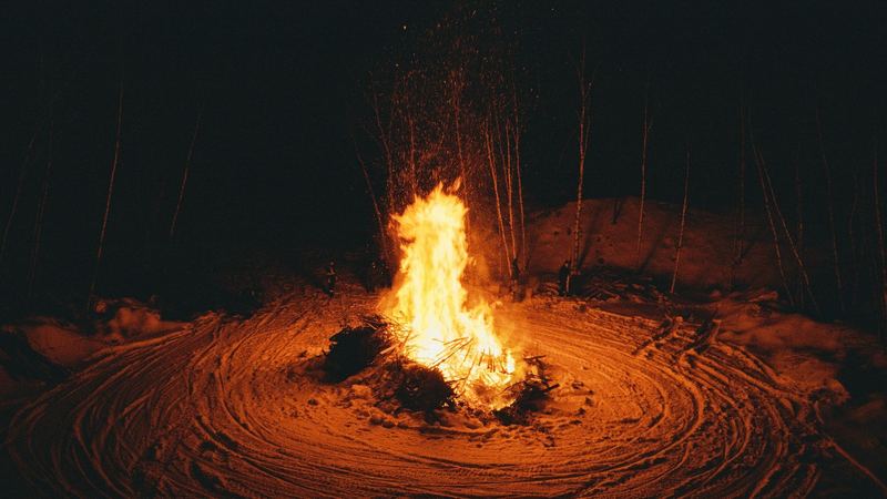 A great bonfire throwing sparks into the night above a ring of trodden snow among birches