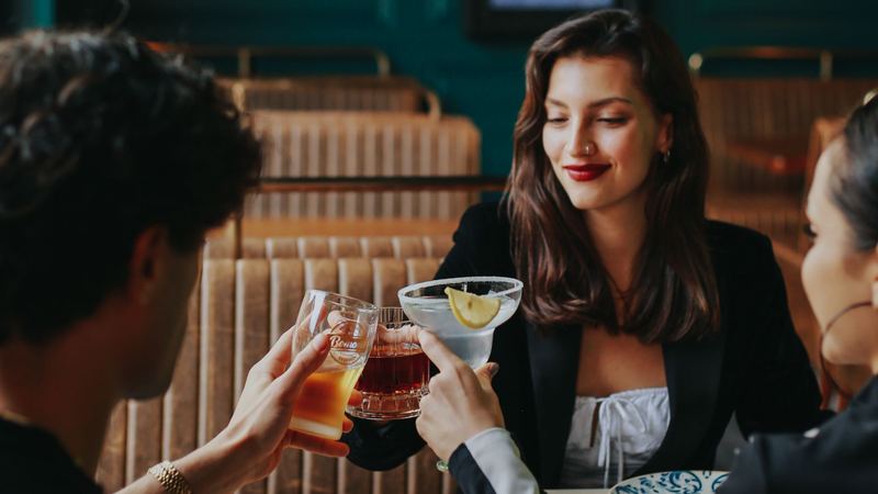 Friends raising cocktails across a table in a restaurant with green panelled walls