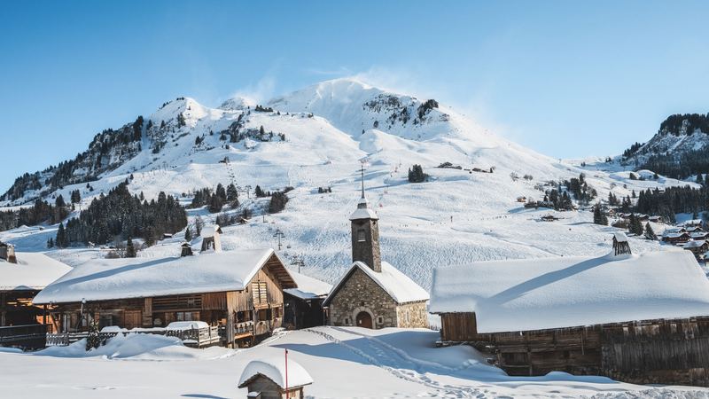 Snow-covered chalets and a stone chapel below the white slopes, Courchevel