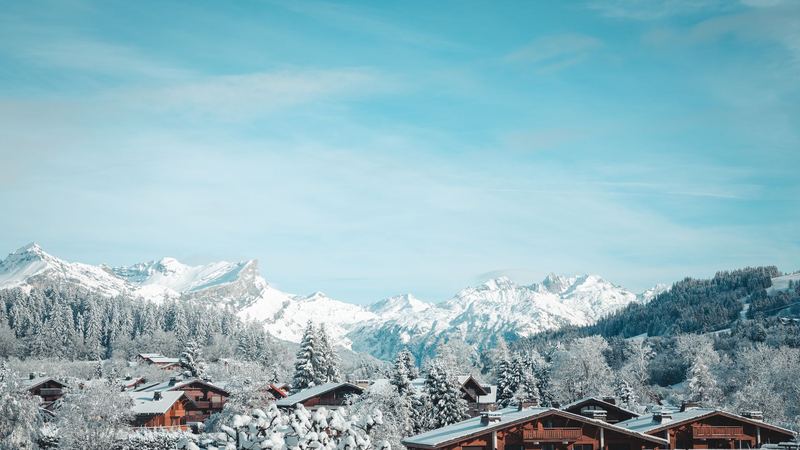 Snow-laden chalets and forest below the mountains, Megève