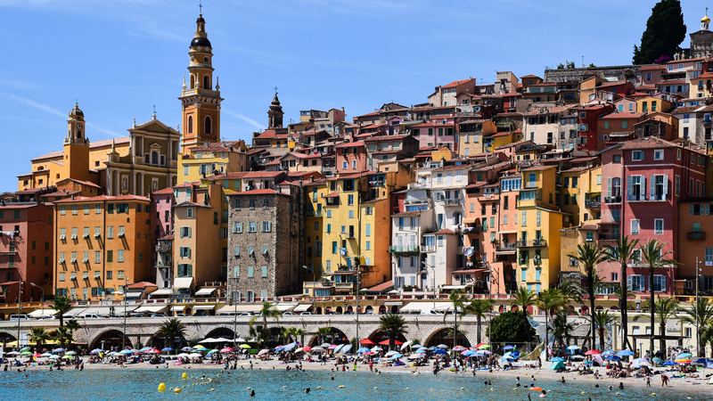 The ochre and pink old town of Menton below the bell tower of Saint-Michel, palms along the harbour
