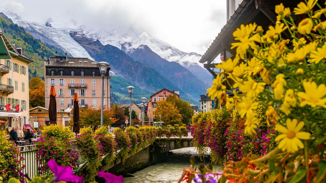 Yellow and pink flowers along the river in Chamonix, with grand hotels and the glaciers of Mont Blanc beyond