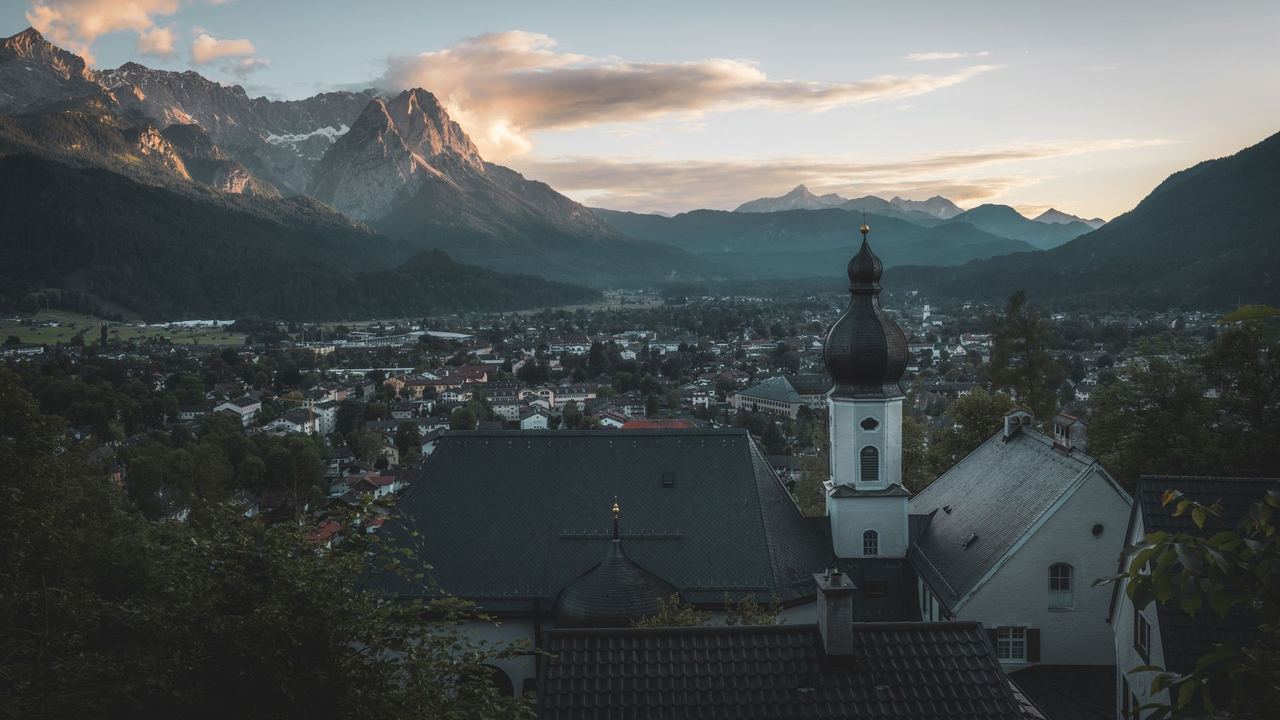 Garmisch-Partenkirchen in its valley at dusk below the Alpspitze and the Waxenstein, an onion-domed church tower in front