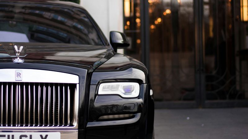A black Rolls-Royce at the glass doors of a grand entrance