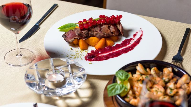 Pink slices of venison on golden squash with redcurrants and a berry sauce, a glass of red wine beside it