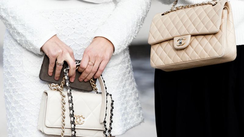 Two women in white tweed jackets and pearls carrying quilted leather handbags