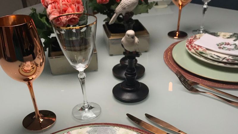 A dinner table laid with rose-gold and crystal glasses, roses and painted winter china
