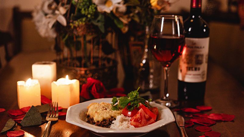 A dinner plate, red wine, candles and rose petals on a table by candlelight