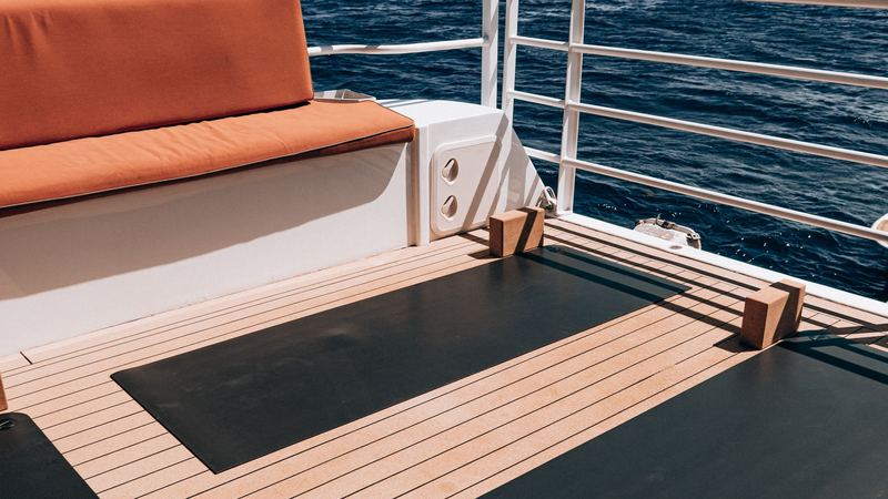 Yoga mats laid out on the teak aft deck of a yacht above the open sea