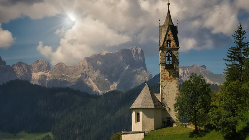 The bell tower of a small chapel on a green hill before the Dolomites, Alta Badia
