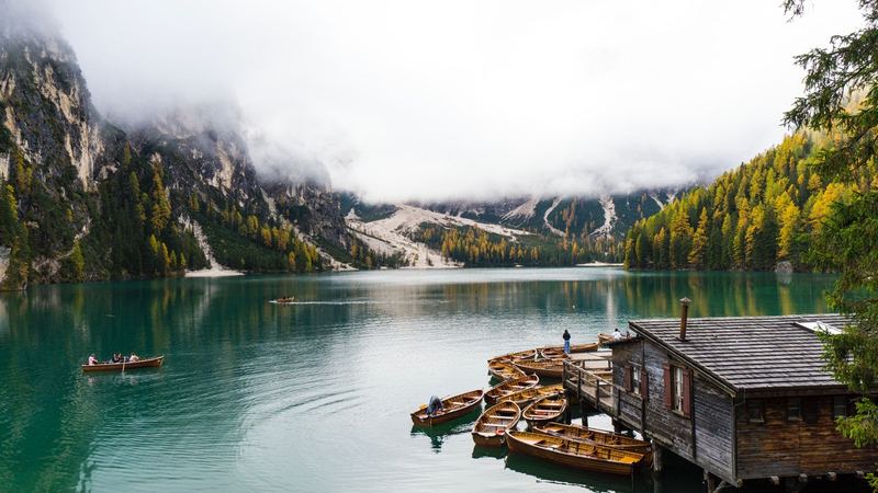 Wooden rowing boats at the boathouse on the green water of Lago di Braies, below larch woods