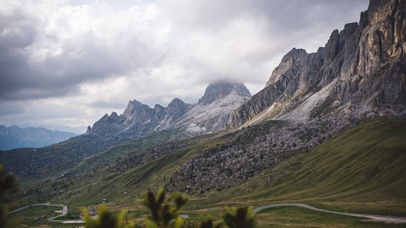 The Giau Pass road winding through green pastures below the Dolomite walls