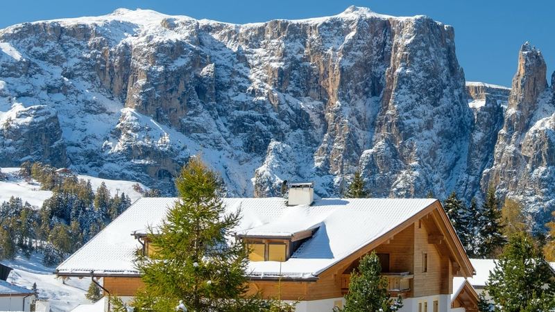 Snow-covered chalets below the Sciliar and its pinnacles under a deep blue sky, Alpe di Siusi