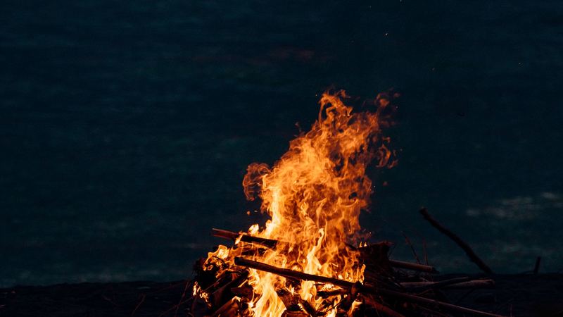 A driftwood bonfire on the shore at night, the dark sea behind it
