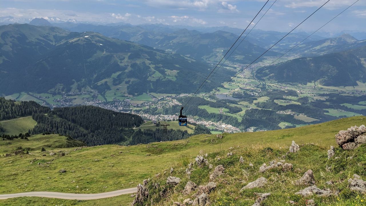 A cable car above the green summer slopes of the Kitzbüheler Horn, with Kitzbühel in the valley below