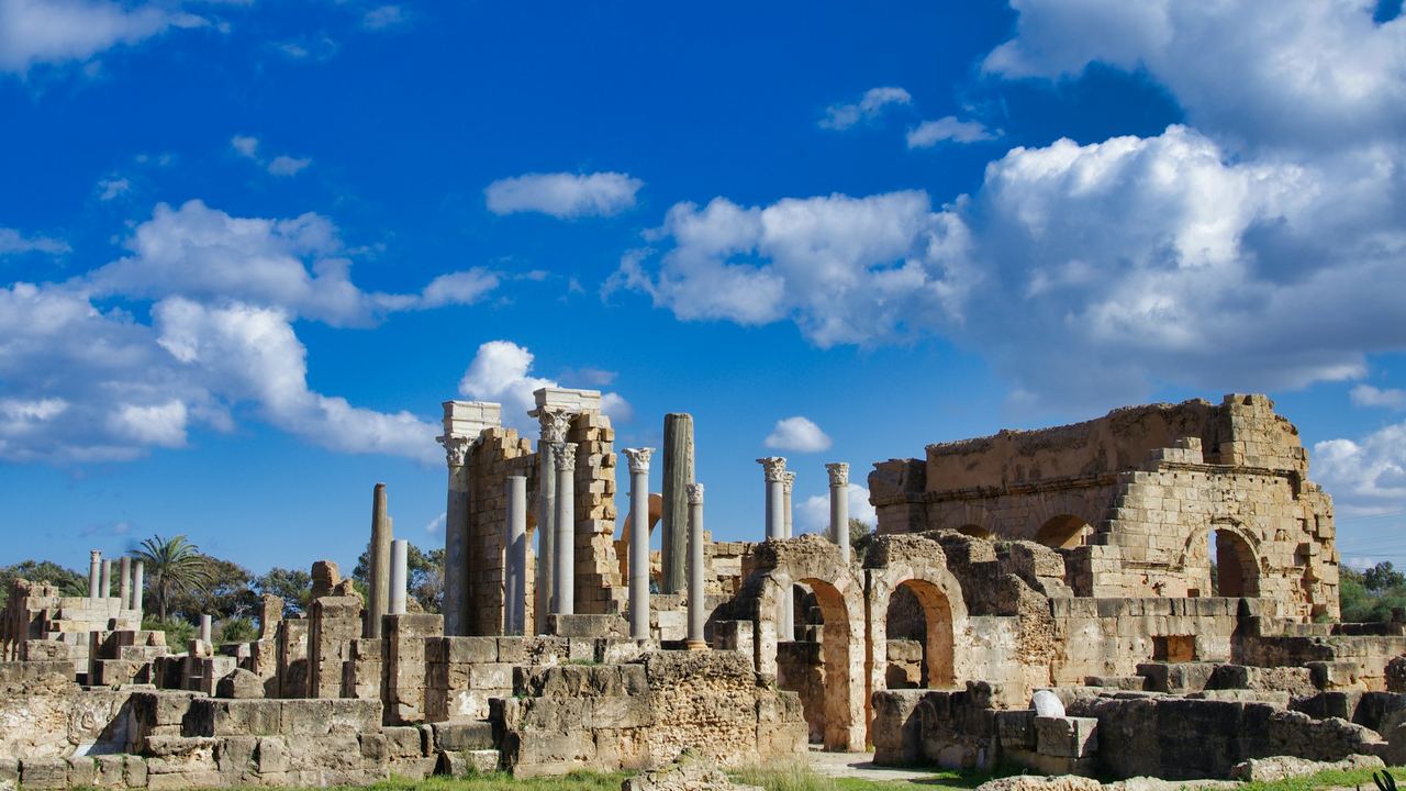 The Roman baths and columns of Leptis Magna under a blue sky with white clouds