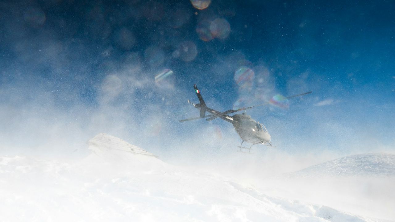 A helicopter lifting off from the snow on a high Alpine ridge