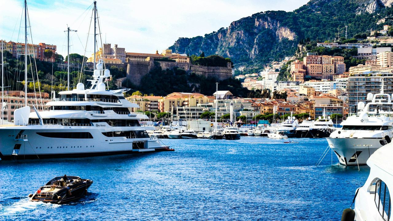 A superyacht in Port Hercule below the Prince’s Palace, a Riva crossing the harbour