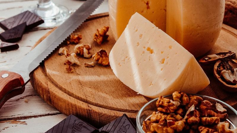 A wheel of mountain cheese cut on a wooden board, walnuts, dark chocolate and a glass of red wine
