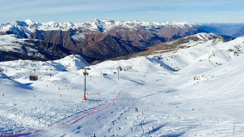 Wide groomed pistes and chairlifts below snowy peaks under a deep blue sky in the Three Valleys