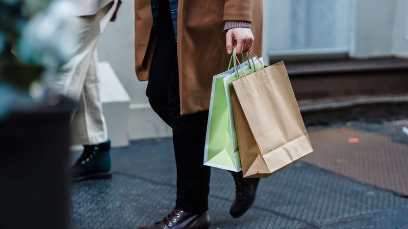 A shopper in a camel coat walking with paper shopping bags