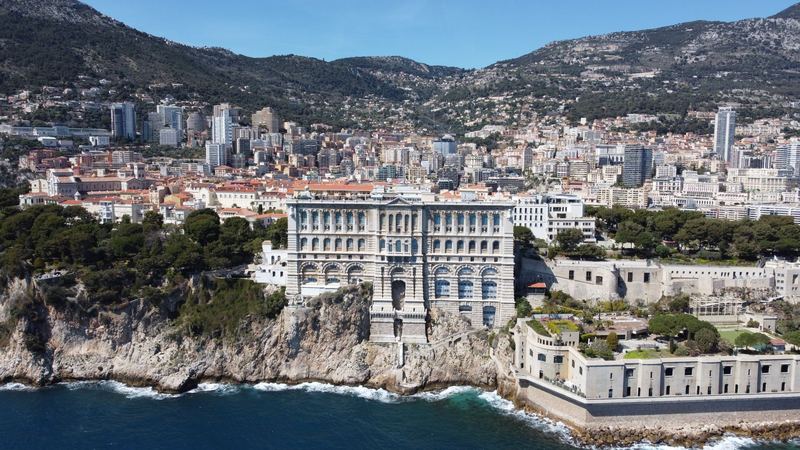 The Oceanographic Museum rising from the cliff above the sea, with Monaco and the mountains behind, seen from the air