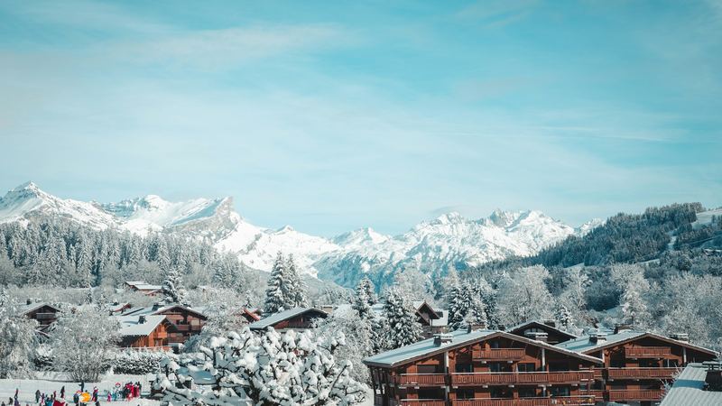 Timber chalets of Megève among snow-laden trees, with the snowy peaks beyond under a blue sky