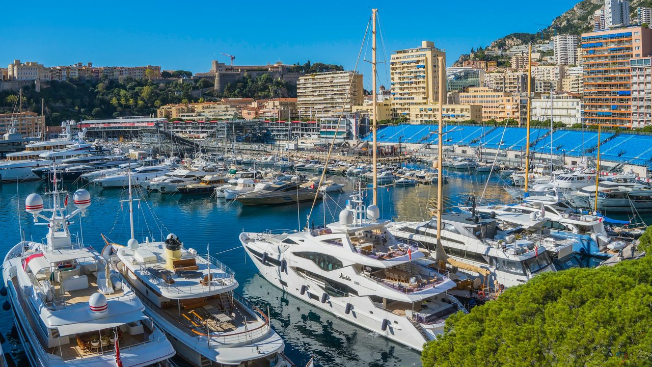 Superyachts moored in Port Hercule below the Rock and the Prince’s Palace, Monaco, under a clear blue sky
