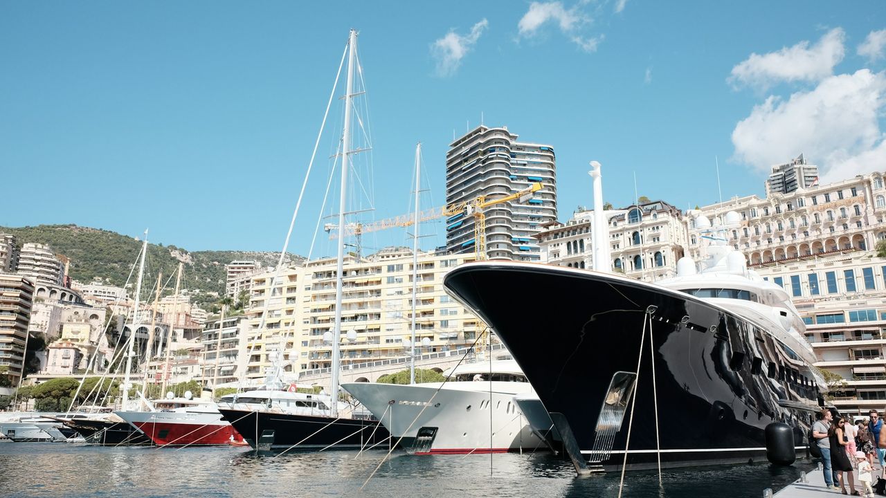 The black bow of a superyacht moored stern-to among sailing yachts in Port Hercule below Monte-Carlo