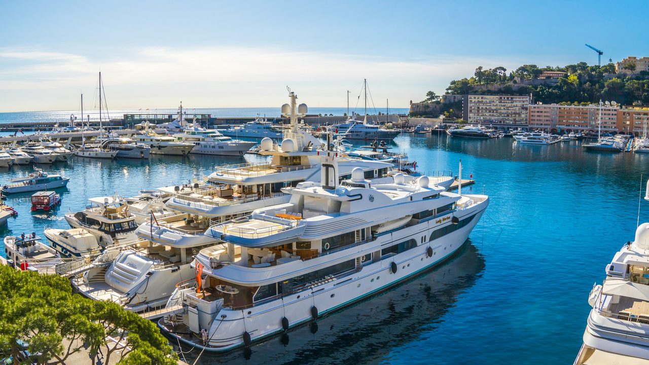 Superyachts moored in the blue water of Port Hercule, Monaco, below the Rock and the old town