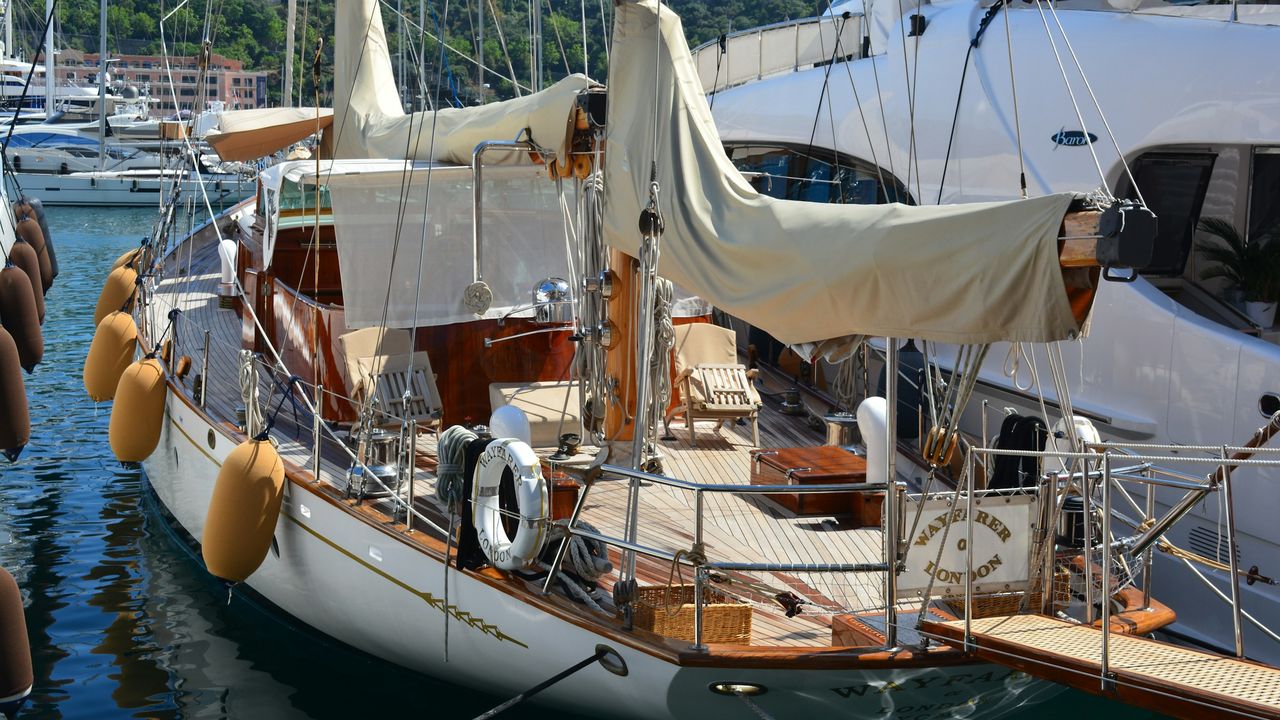 The varnished teak deck, furled sails and golden fenders of the classic ketch Wayfarer of London, moored in Port Hercule below the Rock