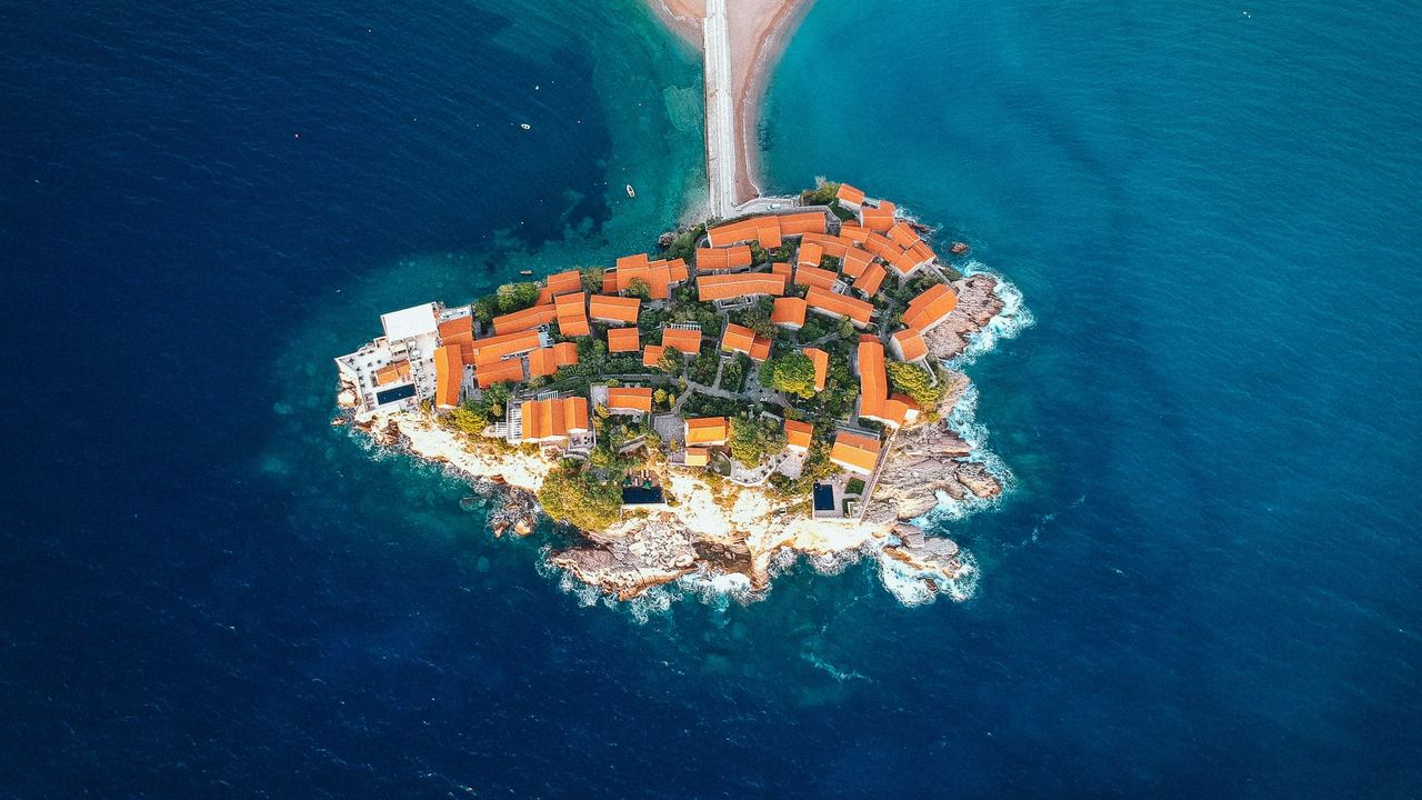 The island village of Sveti Stefan and its causeway seen from above, ringed by deep blue sea