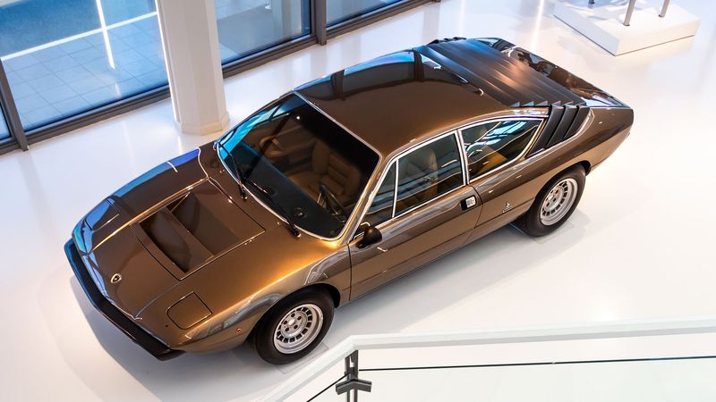A bronze Lamborghini Urraco of the 1970s seen from a staircase above a museum floor