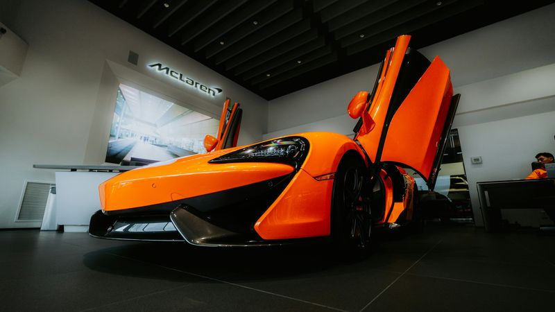 An orange McLaren with its doors raised, in a McLaren showroom