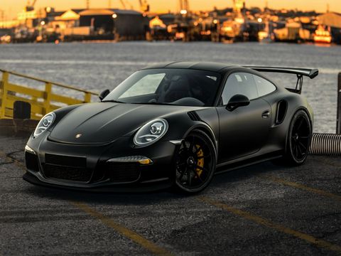 A matt-black Porsche 911 GT3 RS on a harbour quay at sunset