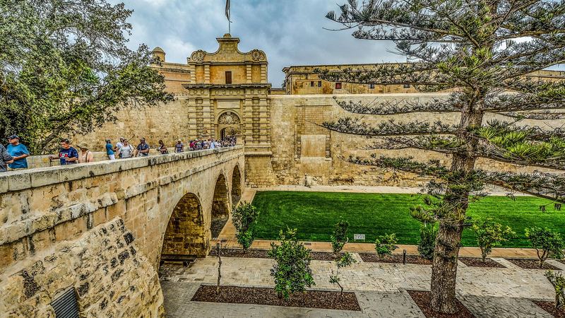 The stone bridge and Baroque gate leading into the walled city of Mdina, above a green moat garden