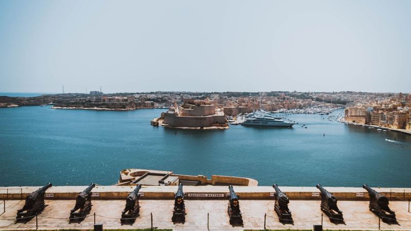 Cannons of the Saluting Battery above the Grand Harbour, with Fort St Angelo and superyachts in the marina at Birgu across the water