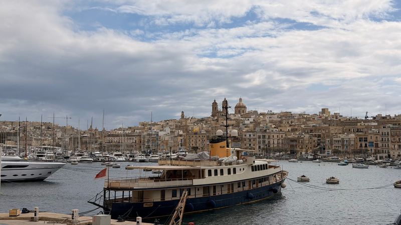 A classic motor yacht moored in the marina below the honey-coloured houses and church domes of the Three Cities