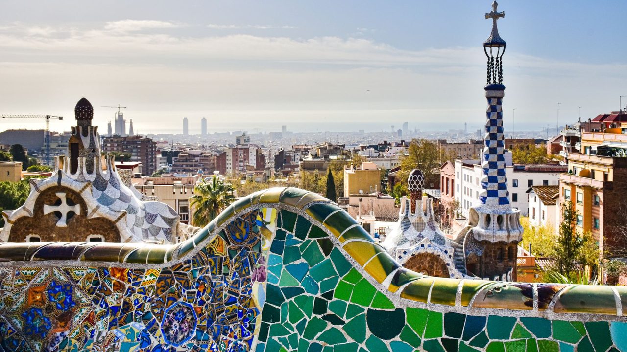 Gaudí's mosaic bench and gatehouse spire in Park Güell, Barcelona and the sea beyond