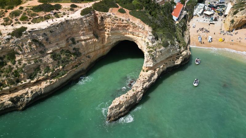 Turquoise water beneath the golden cliffs and sea arch at Benagil, near Porches in the Algarve, seen from the air