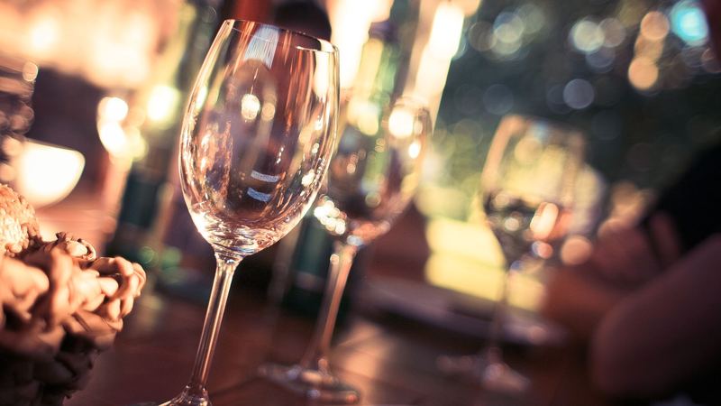Wine glasses on a candlelit dinner table, with warm lights glowing behind